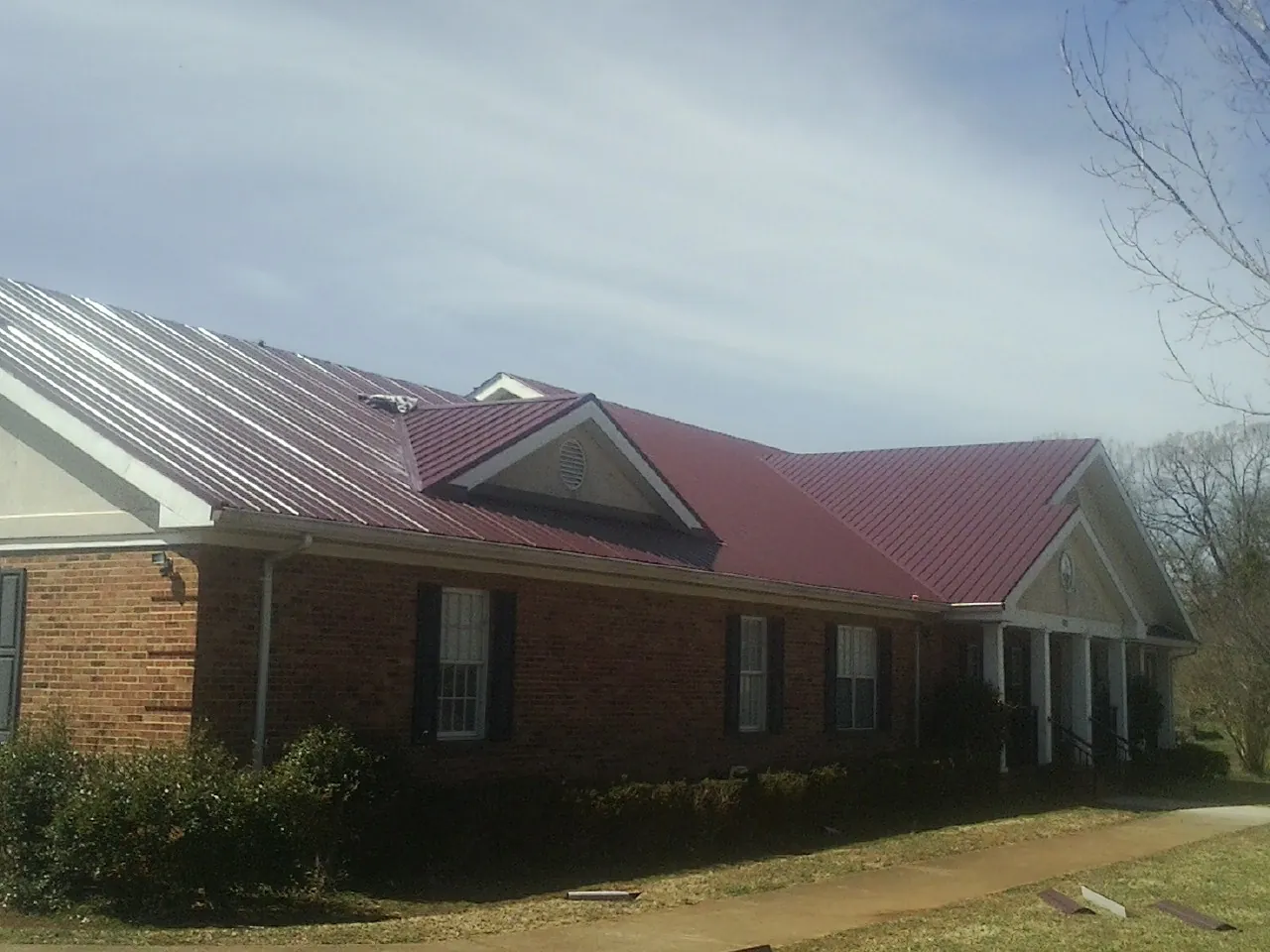 Red metal roof with gabled entries on a long brick building, from a Hail Damage Roof Repair job in Harpers Ferry