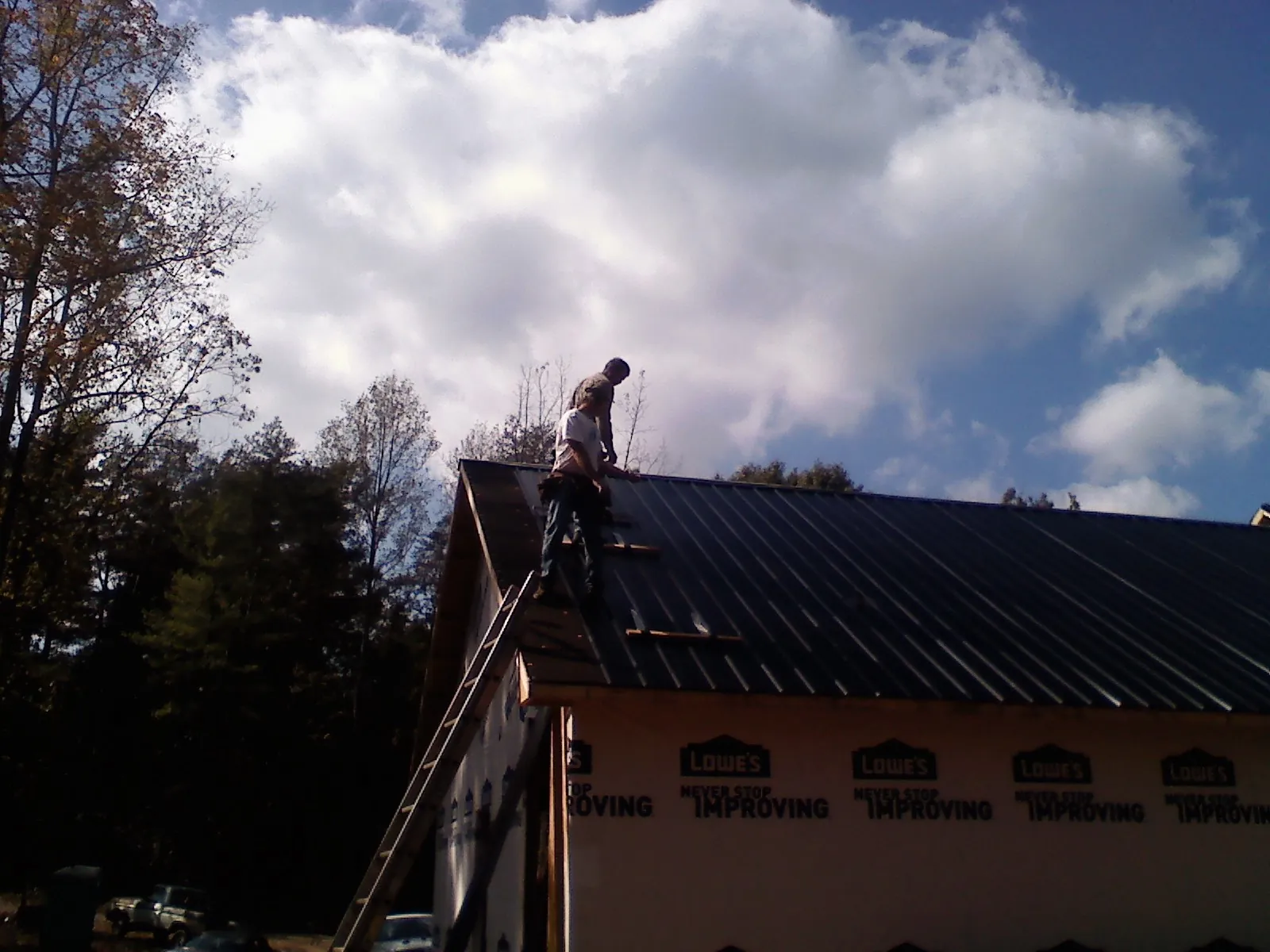 Roofer fastening dark metal panels high against a cloudy sky, from a Roof Inspection job in Harpers Ferry