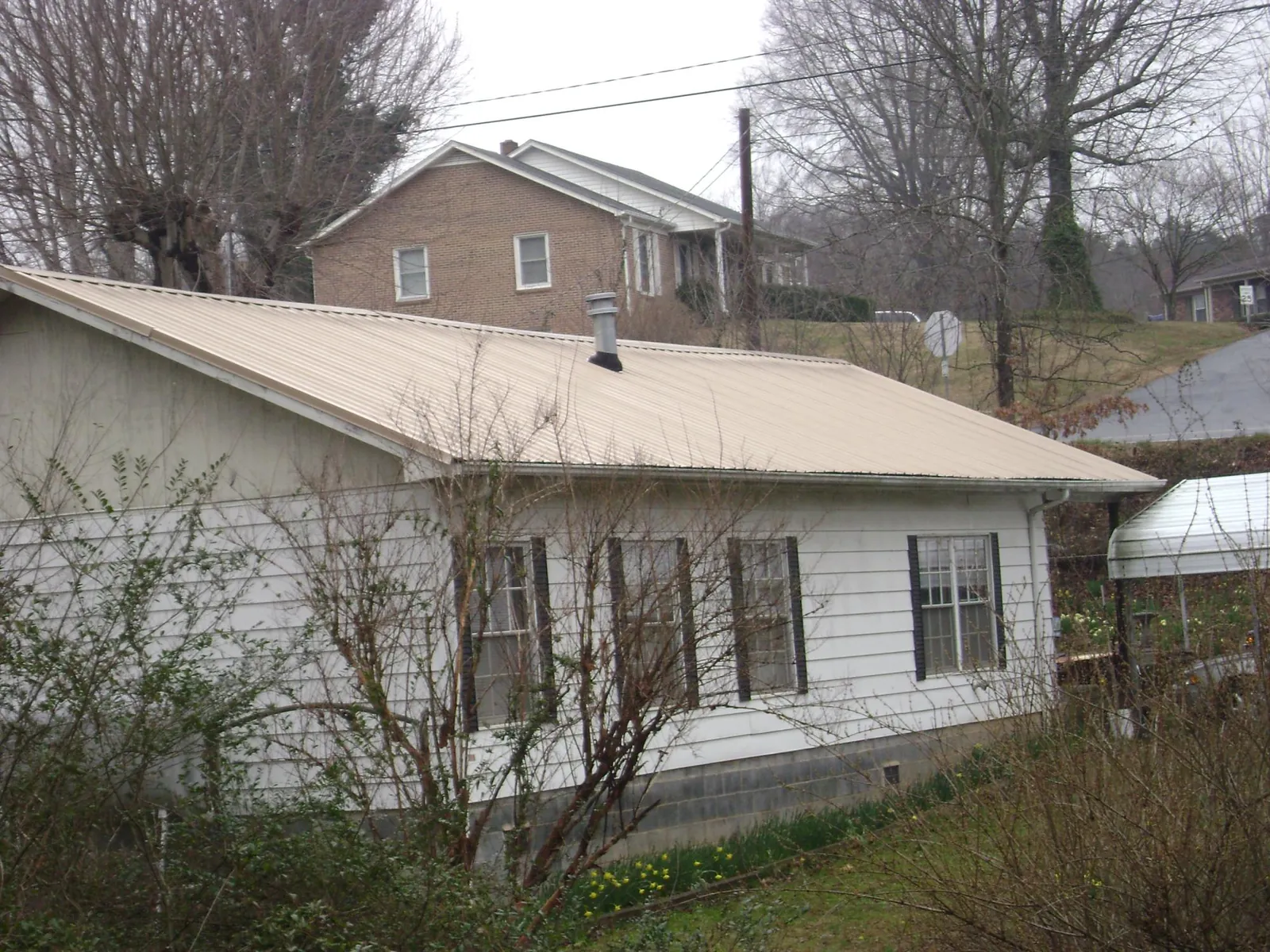 Tan metal roof on a white sided house set into a hillside — Commercial Roofing by Roofing Brothers in Harpers Ferry
